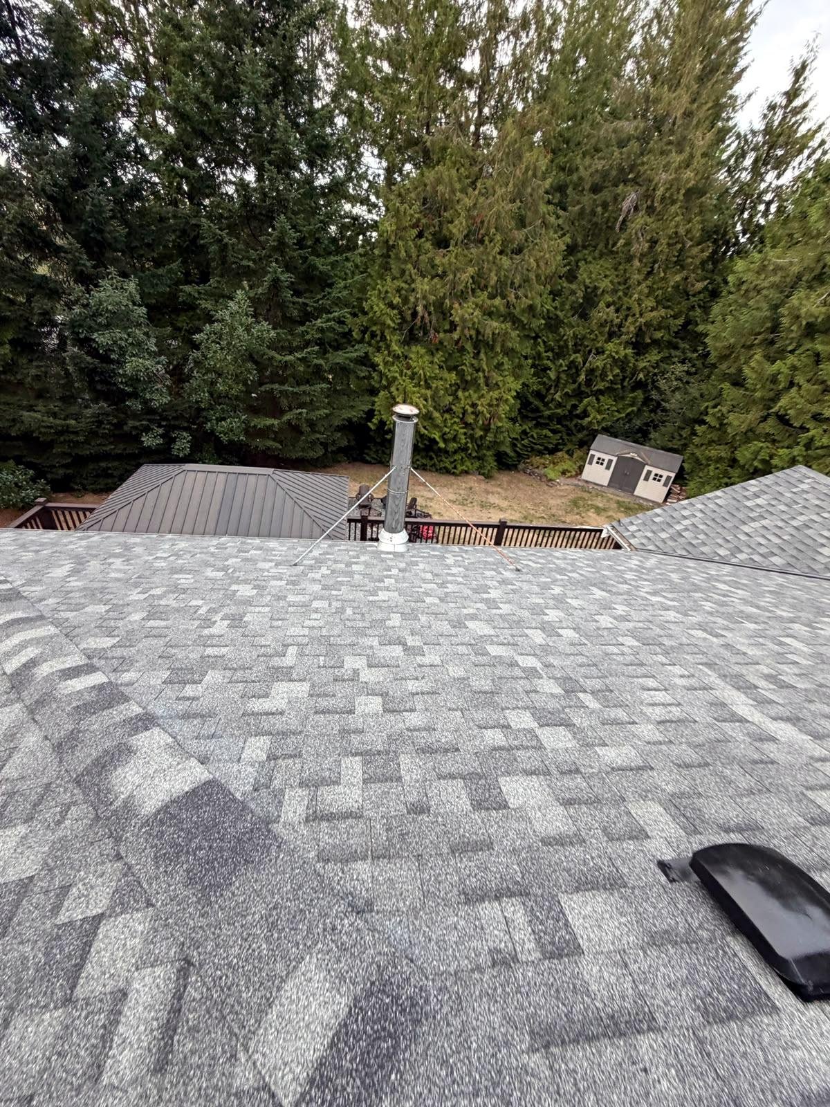Aerial view of a completed shingle roof surrounded by forest in Parksville